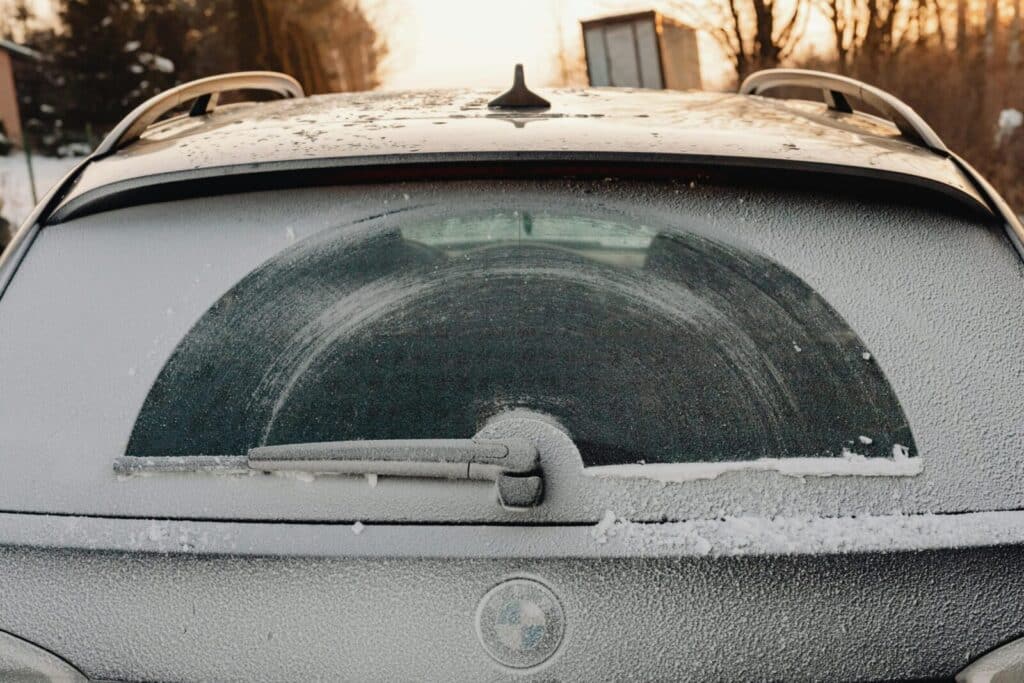 Close-up of a frosted car rear window showing unique patterns created by snowfall and a wiper.