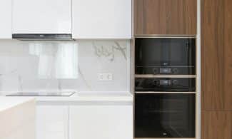 Modern interior of white and wooden kitchen with cabinets cupboards and built in appliances in contemporary flat