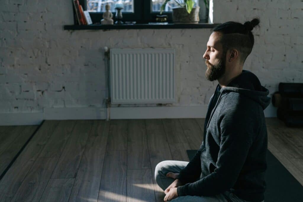 Side view of a man meditating indoors in a serene environment, promoting mental wellness and tranquility.