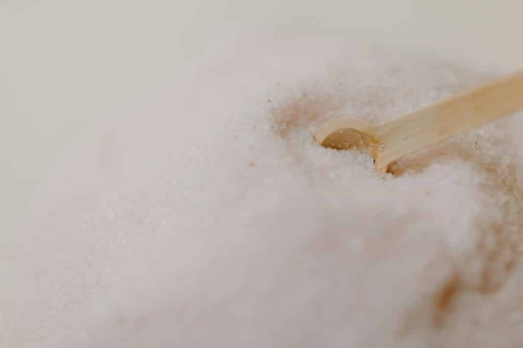 A detailed close-up of pink Himalayan salt with a wooden spoon on a smooth surface.