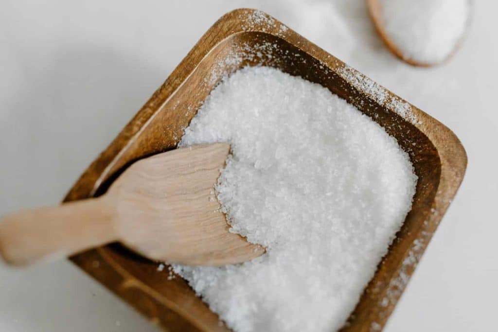 Close-up of coarse sea salt in a wooden bowl with a wooden scoop, perfect for culinary use.