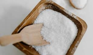 Close-up of coarse sea salt in a wooden bowl with a wooden scoop, perfect for culinary use.