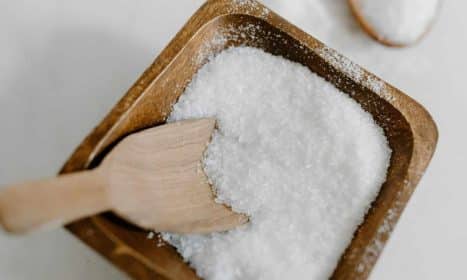 Close-up of coarse sea salt in a wooden bowl with a wooden scoop, perfect for culinary use.