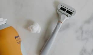 Top view of a razor and shaving foam on a marble surface, perfect for grooming and lifestyle themes.