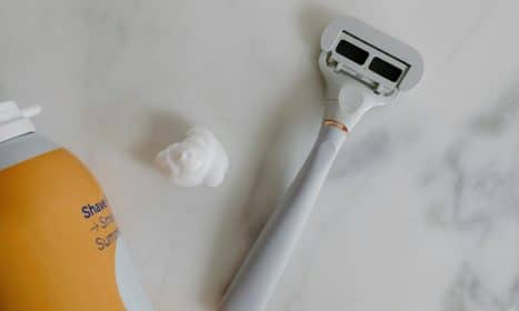Top view of a razor and shaving foam on a marble surface, perfect for grooming and lifestyle themes.