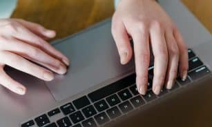 From above of crop person using touchpad of laptop while browsing internet sitting near wooden table
