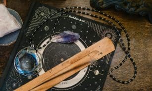 Astrology-themed flat lay featuring a birthdate book, crystals, and necklace on a wooden surface.