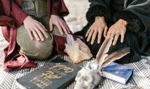 A mystical scene with crystals, a skull, books, and hands in contemplative poses.