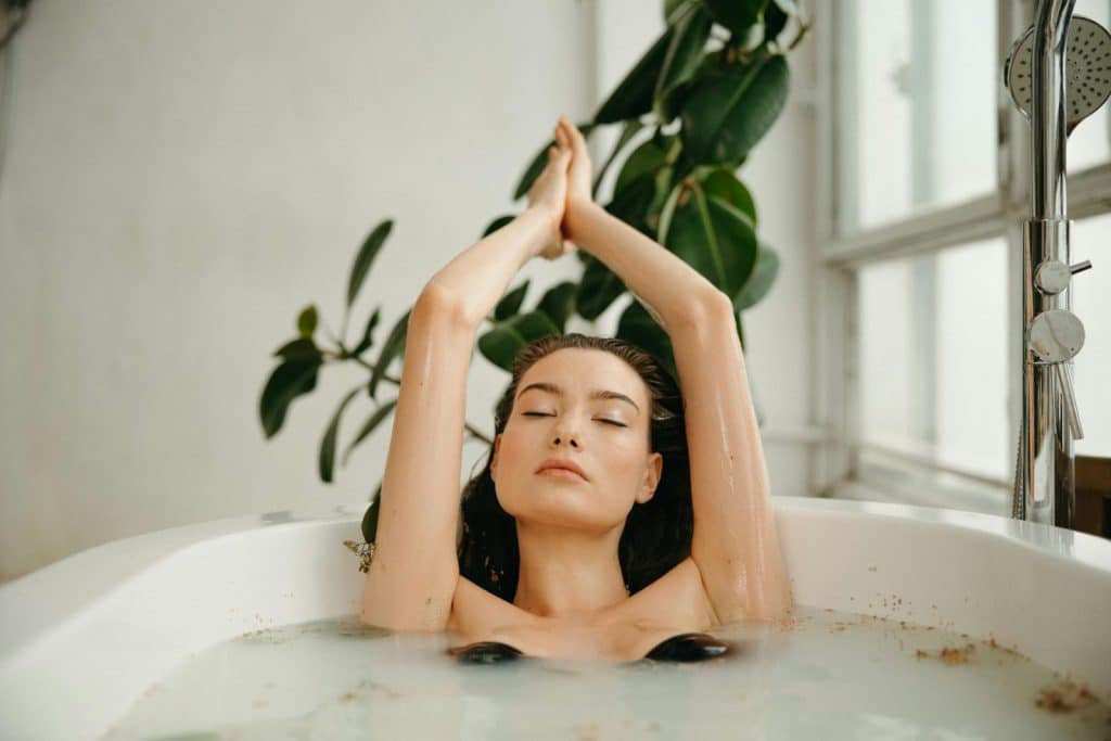 Serene woman in a bathtub, practicing self-care and relaxation amid tranquil surroundings.