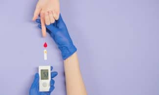 Gloved hand testing blood glucose level with meter and blood drop.