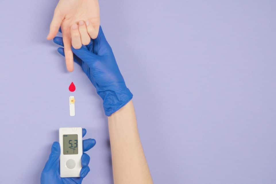 Gloved hand testing blood glucose level with meter and blood drop.