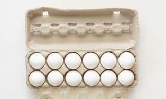 Minimalist flat lay of white eggs in a carton tray, perfect for culinary or health concepts.
