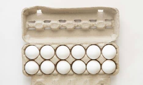 Minimalist flat lay of white eggs in a carton tray, perfect for culinary or health concepts.