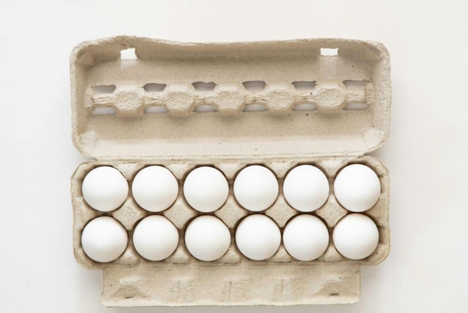 Minimalist flat lay of white eggs in a carton tray, perfect for culinary or health concepts.