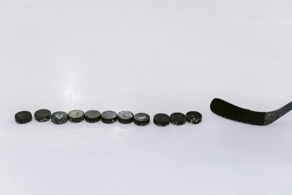 A row of hockey pucks and a stick on an ice rink, perfect for sports content.