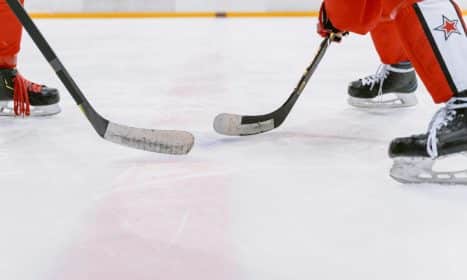 Intense close-up action of ice hockey players competing indoors, focusing on their sticks and skates.