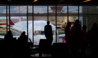 Silhouettes of travelers waiting at an airport terminal with an airplane visible through the window.
