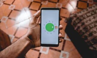 Close-up of a hand holding a smartphone displaying Android 11 interface indoors on patterned floor.
