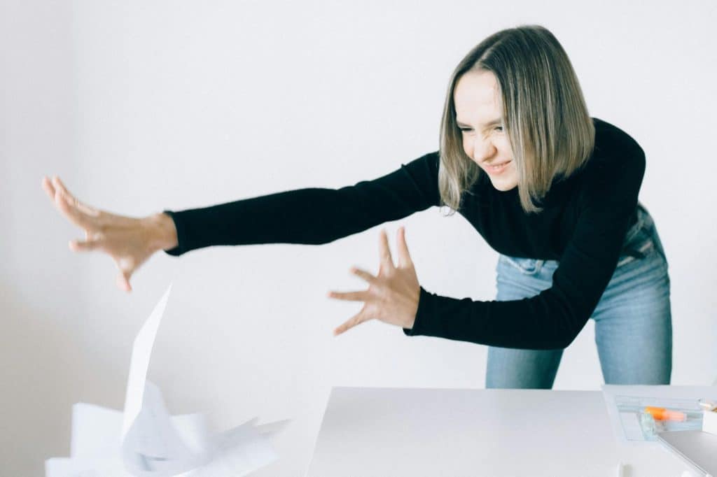 A woman in a black top with short hair energetically tosses papers indoors.