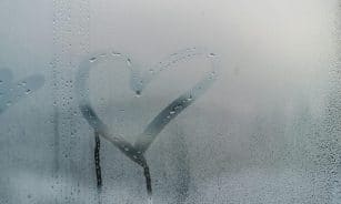 A heart shape drawn on a foggy window with water droplets streaming down for a romantic touch.