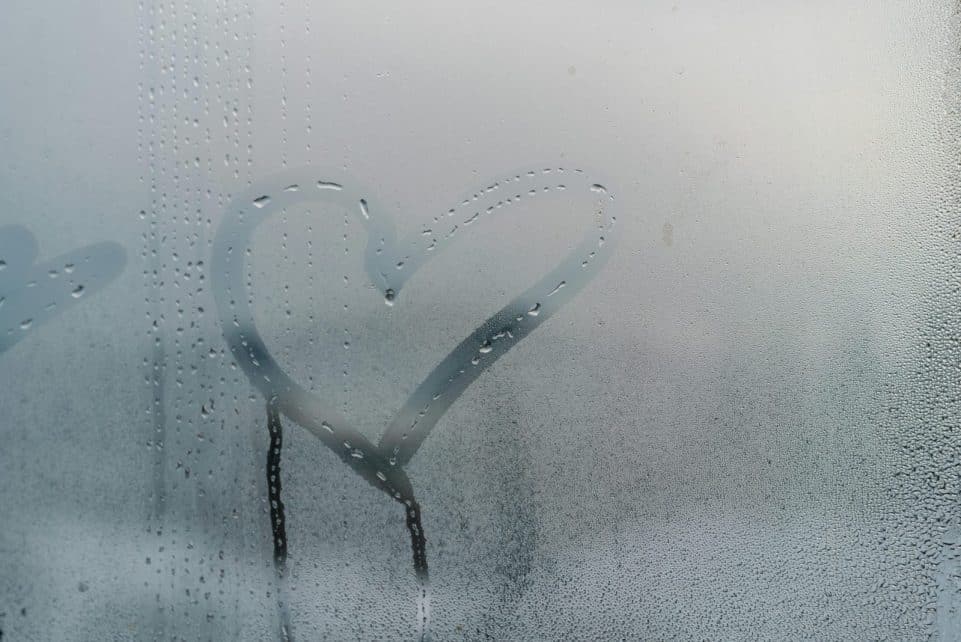 A heart shape drawn on a foggy window with water droplets streaming down for a romantic touch.