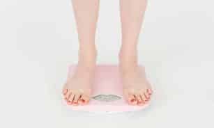 High angle of crop anonymous female measuring weight for control body against white background in studio