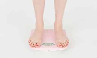 High angle of crop anonymous female measuring weight for control body against white background in studio