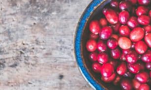 Colorful fresh cranberries in a textured blue bowl on a wooden tabletop creating a rustic and healthy food theme.