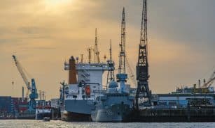 Cargo port scene with ships and cranes at sunset, showcasing industrial and maritime activity.