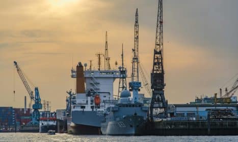 Cargo port scene with ships and cranes at sunset, showcasing industrial and maritime activity.