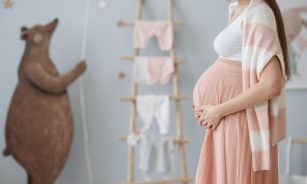 Expectant mother caressing her belly in a cozy nursery room setting, symbolizing love and anticipation.