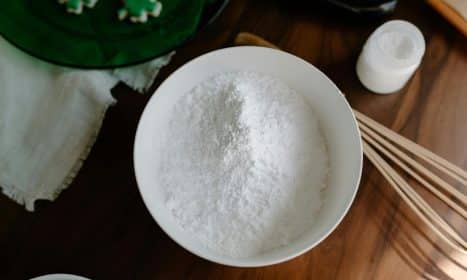 Top view of flour in a bowl with baking utensils on a wooden table, ready for preparation.