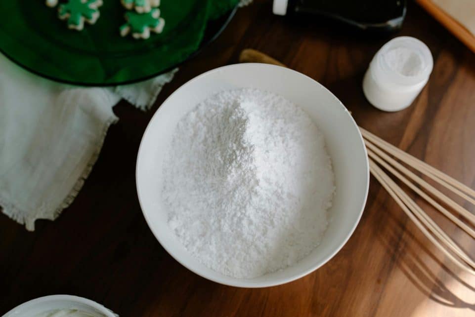Top view of flour in a bowl with baking utensils on a wooden table, ready for preparation.