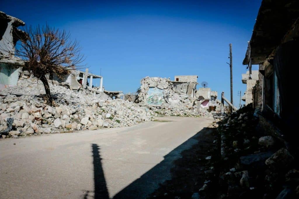 Destroyed buildings and rubble in a deserted street of Idlib, Syria, under clear blue sky.