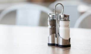 Minimalist salt and pepper shakers set on a wooden table in natural light, showcasing sleek design.