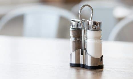 Minimalist salt and pepper shakers set on a wooden table in natural light, showcasing sleek design.