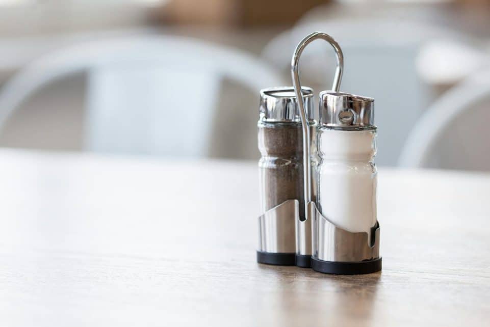 Minimalist salt and pepper shakers set on a wooden table in natural light, showcasing sleek design.