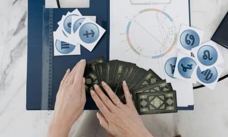 Hands arranging tarot cards with astrology symbols and natal chart on a table.