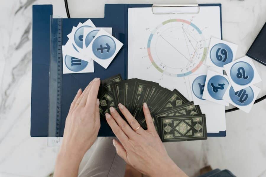 Hands arranging tarot cards with astrology symbols and natal chart on a table.