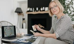Woman with tarot cards using laptop for astrology reading in cozy living room.