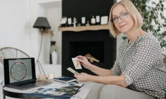 Woman with tarot cards using laptop for astrology reading in cozy living room.