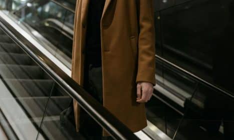Elegant close-up of an adult wearing a brown coat on an escalator, highlighting urban fashion.