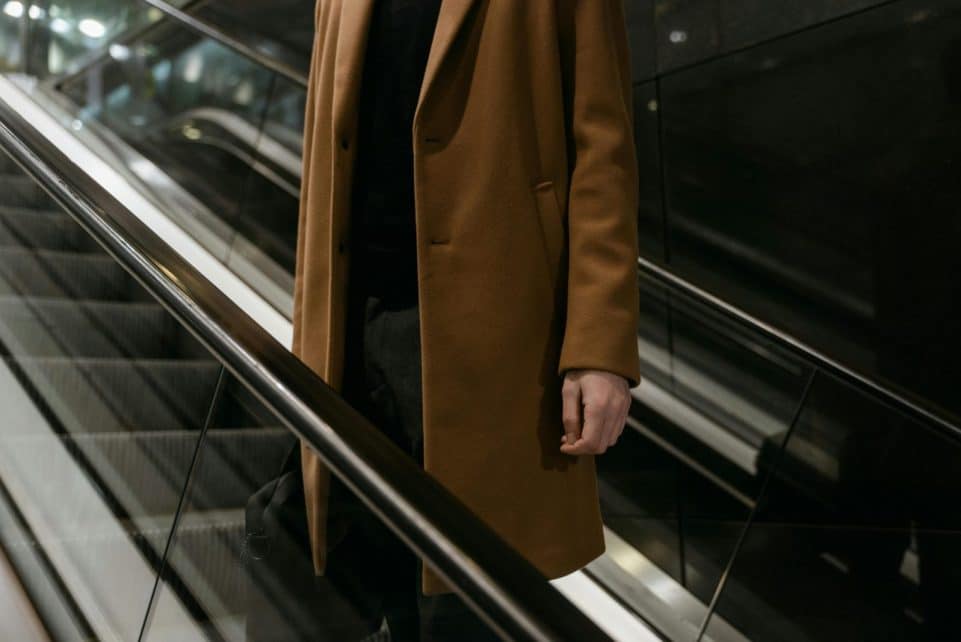 Elegant close-up of an adult wearing a brown coat on an escalator, highlighting urban fashion.