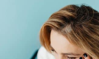 Close-up of a woman with a hand on forehead against a blue background.