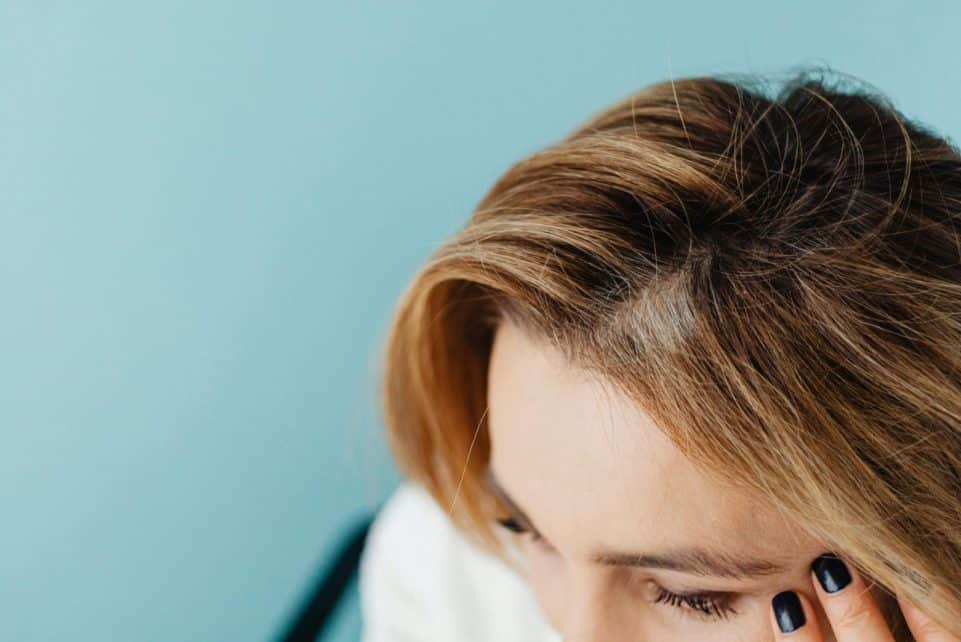 Close-up of a woman with a hand on forehead against a blue background.