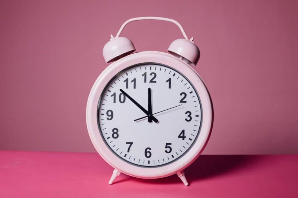 Pink retro alarm clock on a pastel pink background symbolizing time and punctuality.