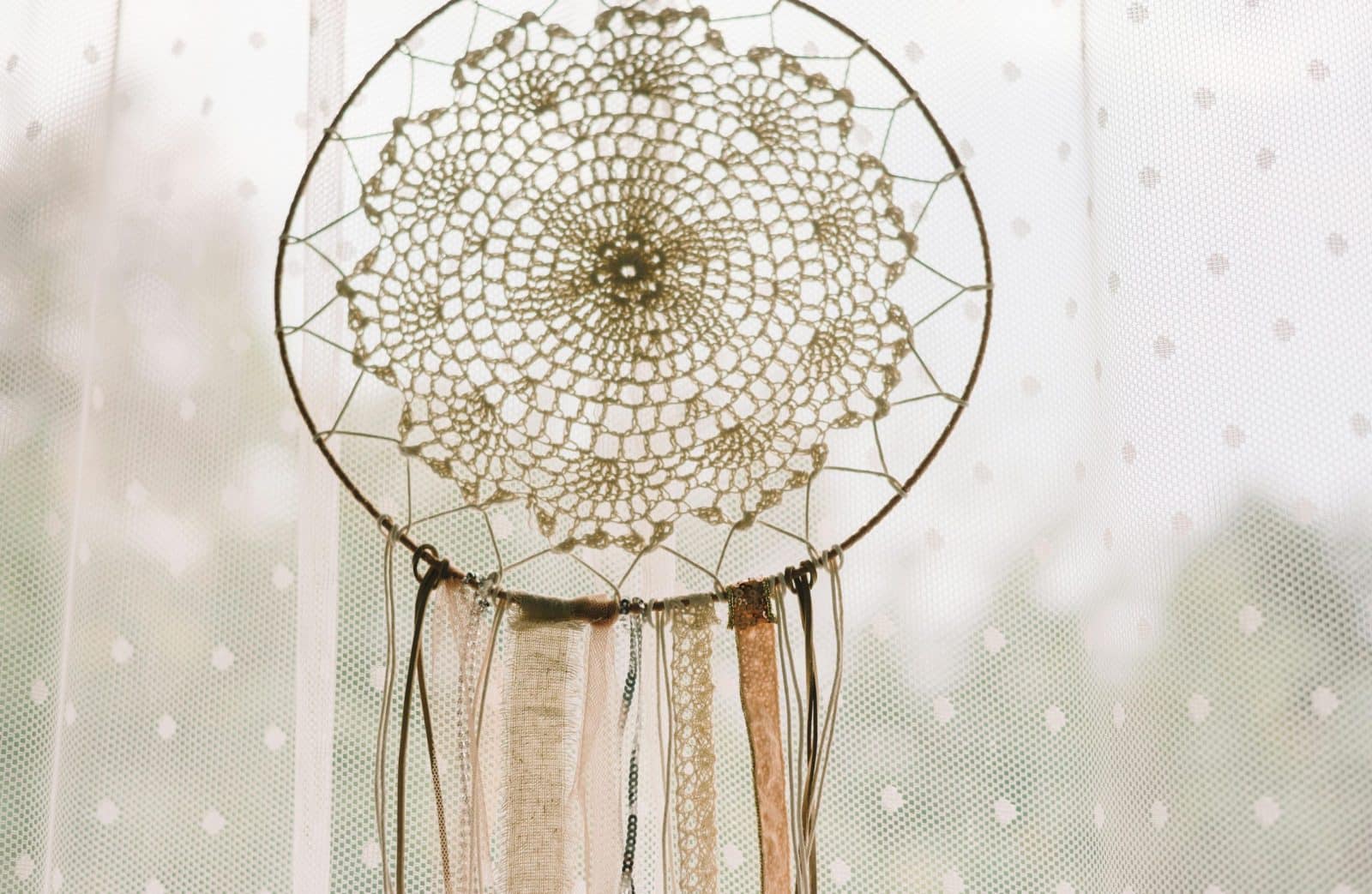 Elegant dream catcher with lace pattern hanging in front of a sheer curtain.