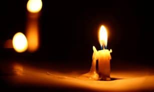 Close-up of a burning candle against a dark background with dripping wax.