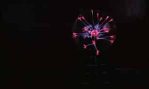 Shiny round glass plasma ball with colorful neon illumination placed in dark room