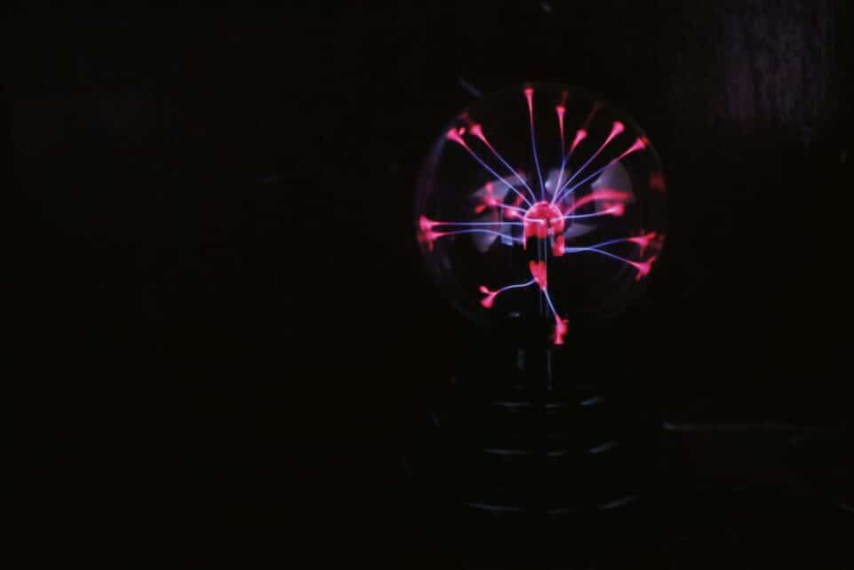 Shiny round glass plasma ball with colorful neon illumination placed in dark room